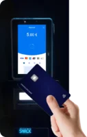 Hand presenting a blue card to an unattended payment terminal screen showing £5.00