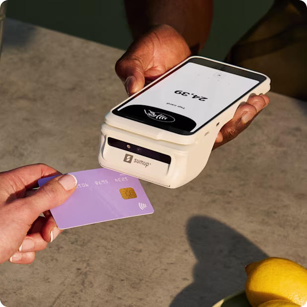 Customer presenting a purple payment card to a white SumUp terminal with printer while the device is held across a counter