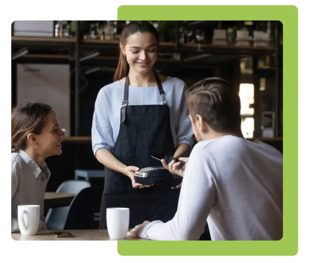 Waitress holding a handheld card machine while a customer pays at a café table